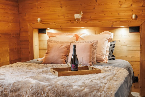 A wooden cabin bedroom with a bed, pillows, a bottle, and a tray.