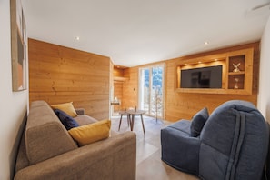 A modern living room with wooden walls, a flat-screen TV, and a dining area with a small table and chairs.