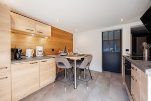 A modern kitchen with wooden cabinetry, a dining table with chairs, and a black door leading to another room.