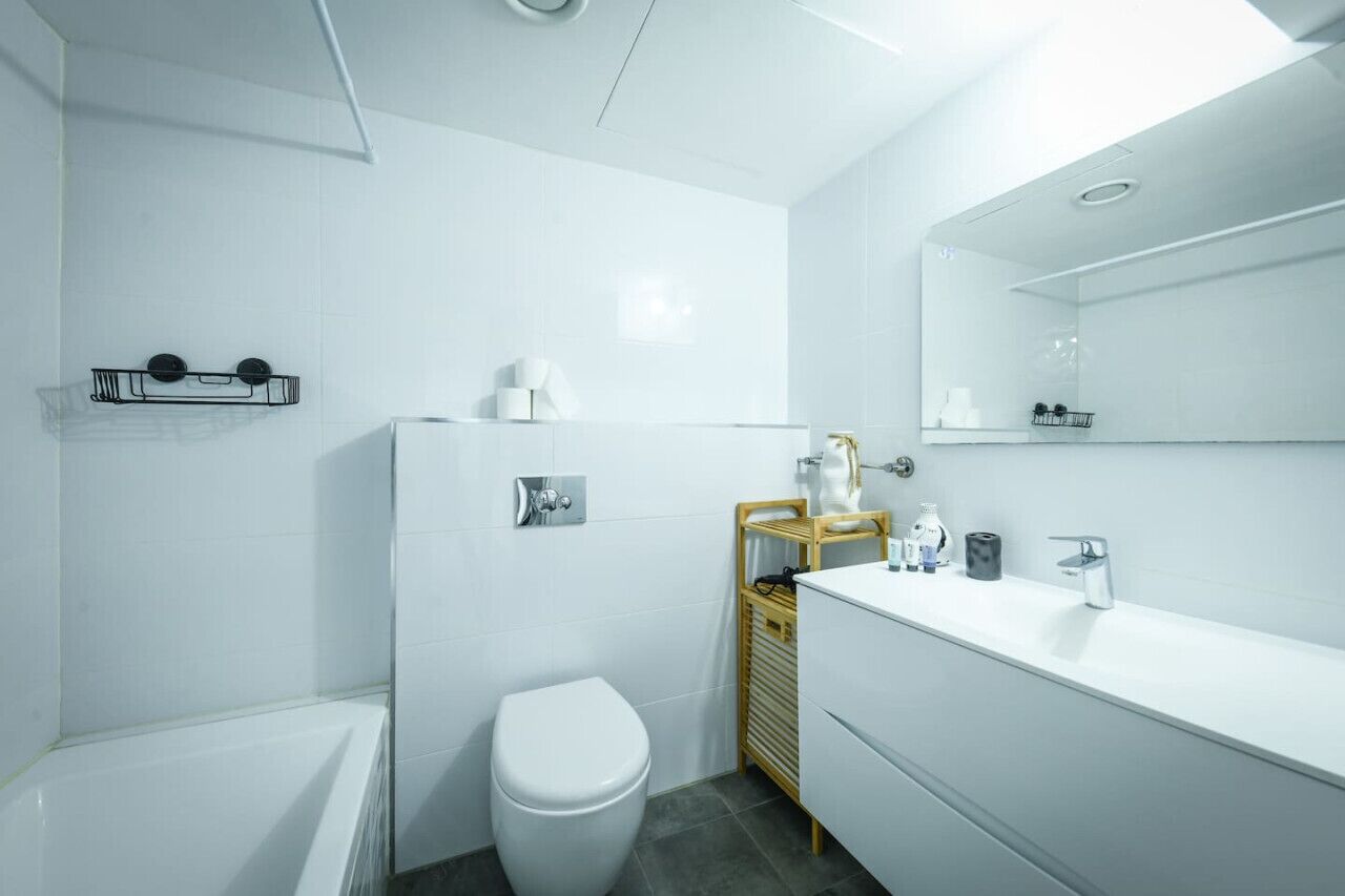 A modern bathroom with a white toilet, a bathtub, a vanity with a mirror, and a towel rack.