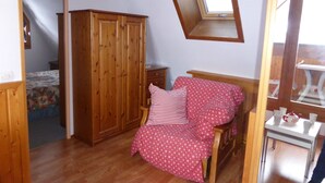 A bedroom with a wooden wardrobe, a bed with a pink polka dot cover, a small bedside table, and a window with a mirror.