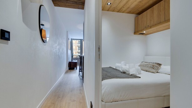 A modern bedroom with a wooden ceiling, a large bed with white bedding, and a view to the outside.