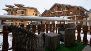 A balcony with wicker furniture, wooden buildings in the background, and a sign indicating a hotel.