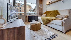 A modern living room with a sofa, a coffee table, a TV, and a large window overlooking buildings.