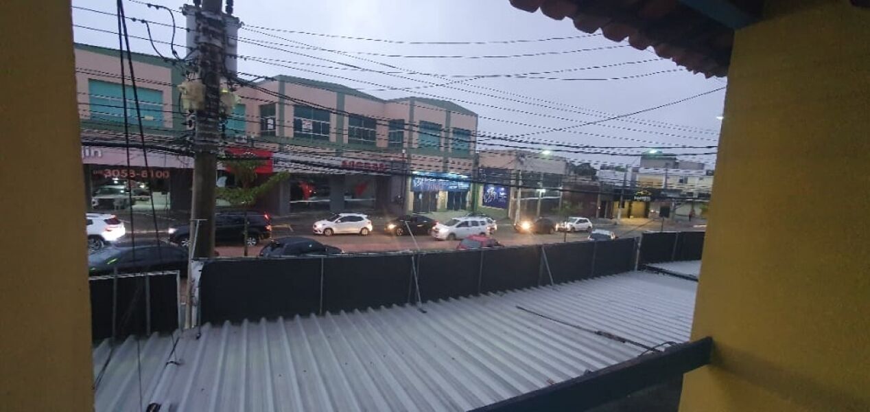 A view from a balcony with a corrugated metal roof overlooking a street with cars and buildings.
