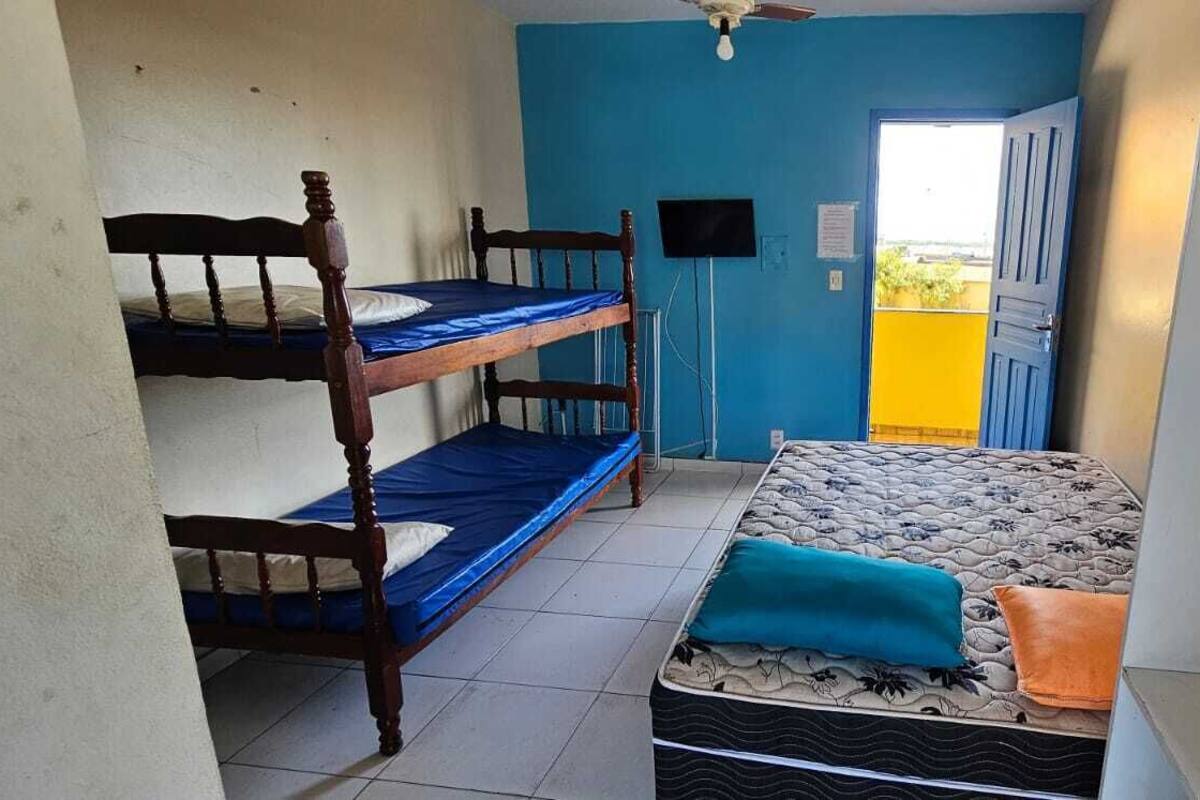 Une chambre de dortoir avec des lits superposés et un lit simple, un ventilateur de plafond et une porte donnant sur l’extérieur.