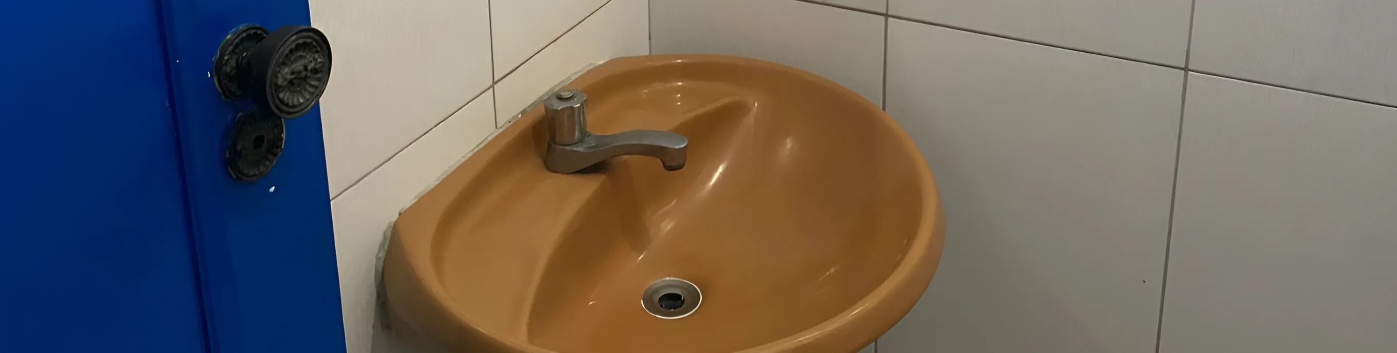 A bathroom with a blue door, a beige sink with a silver faucet, and a drain.