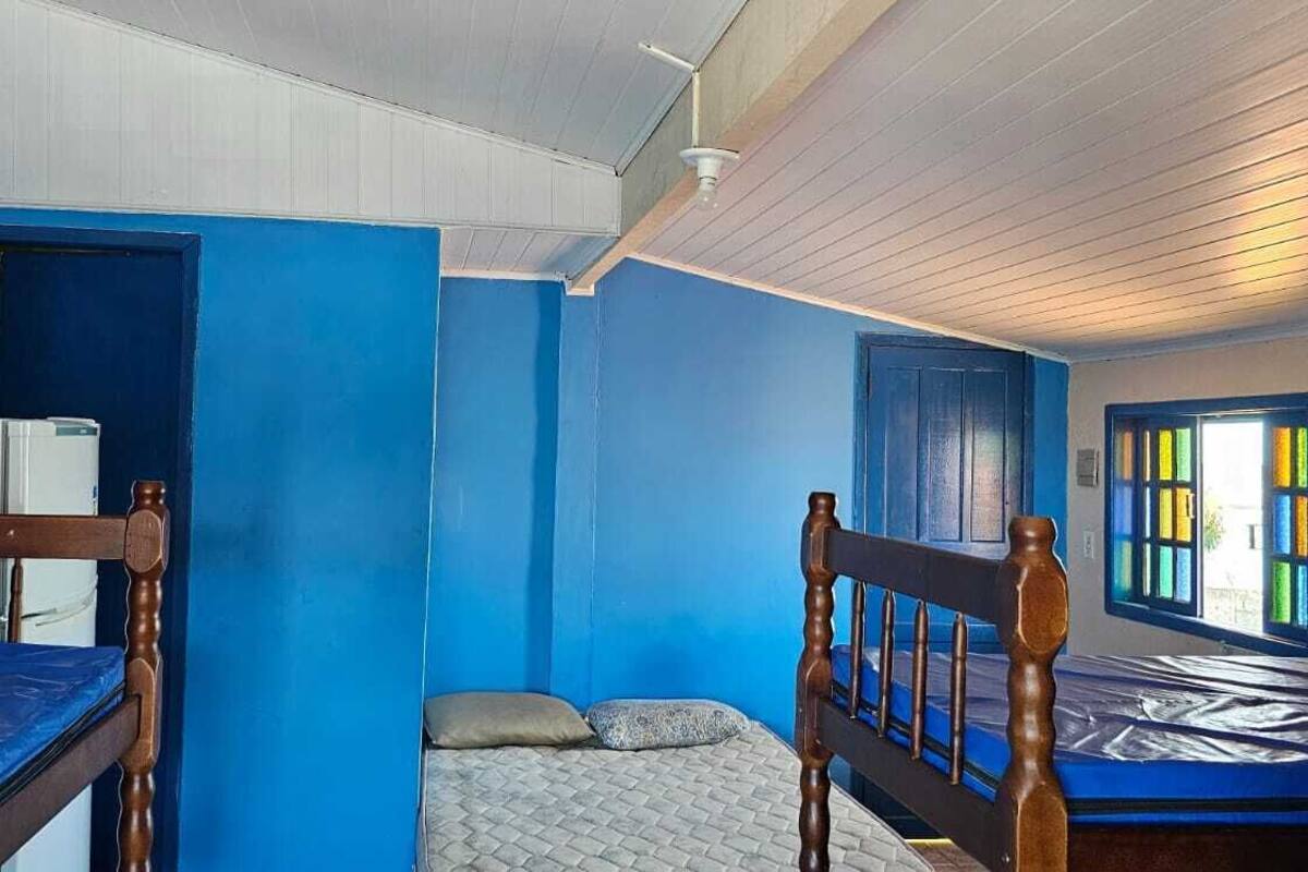 Une pièce avec deux lits superposés en bois, un lit simple, un ventilateur de plafond blanc et une fenêtre ornée de vitraux colorés.
