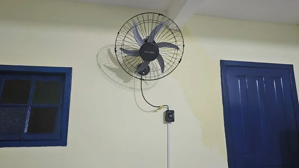 Um ventilador fixado na parede, uma janela com moldura azul e uma porta azul.