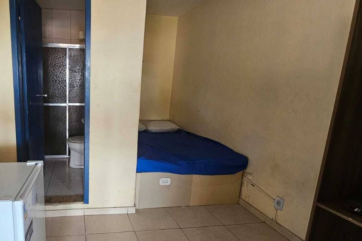 Une petite pièce, de taille modeste, comprenant un lit, un réfrigérateur blanc et une salle de bain avec douche et toilettes.