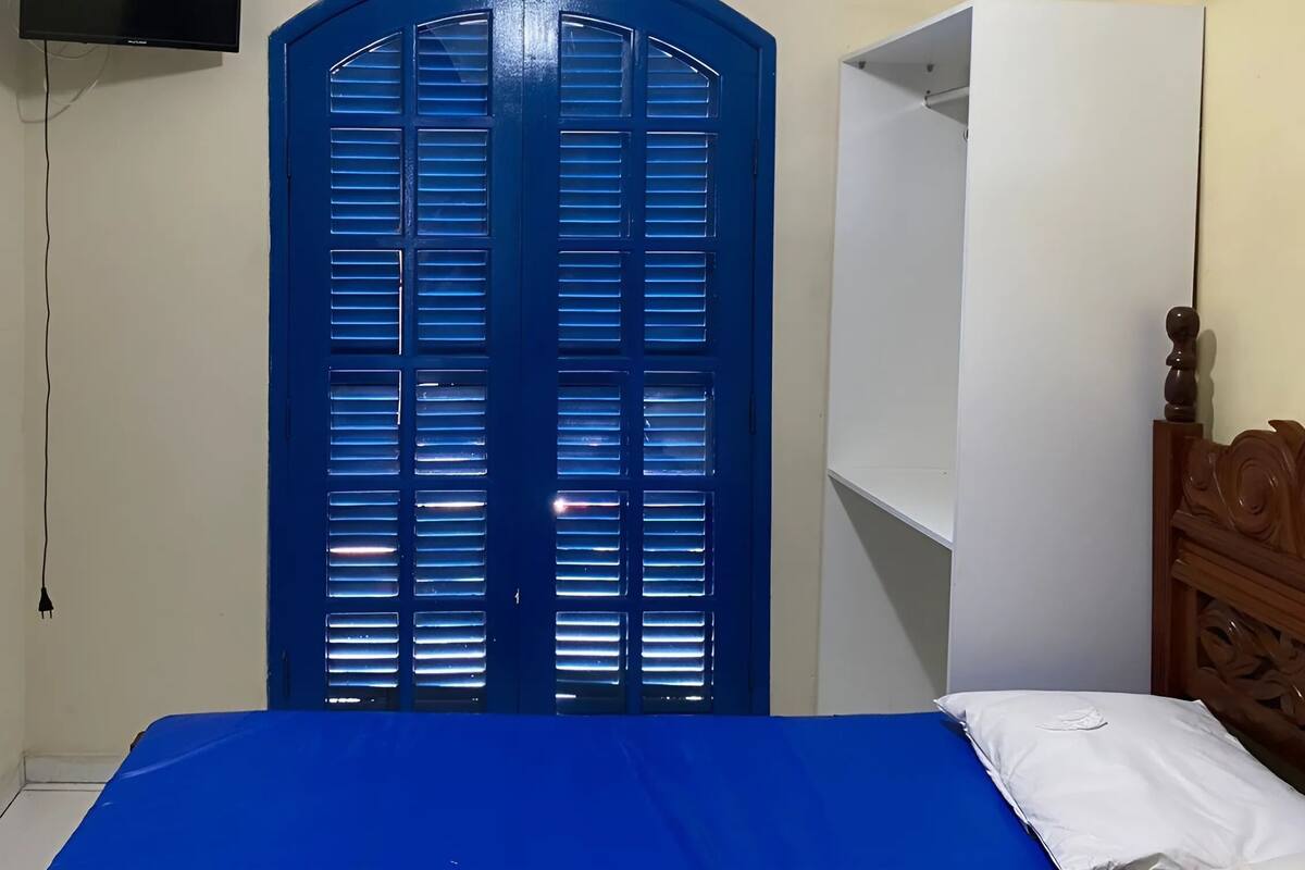 Une chambre à coucher avec une couvre-lit bleue, une tête de lit en bois et une porte bleue à lattes horizontales.