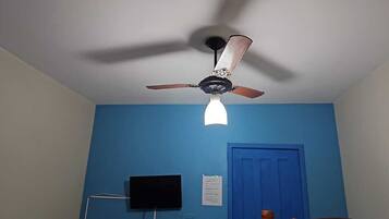 Ein Zimmer mit Deckenventilator, blauer Wand, geschlossener Tür und montiertem Fernseher.