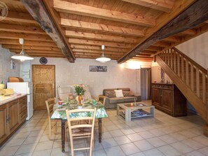 Un intérieur rustique avec un plafond en bois, un coin repas comprenant une table et des chaises, un canapé, une table basse et un escalier.