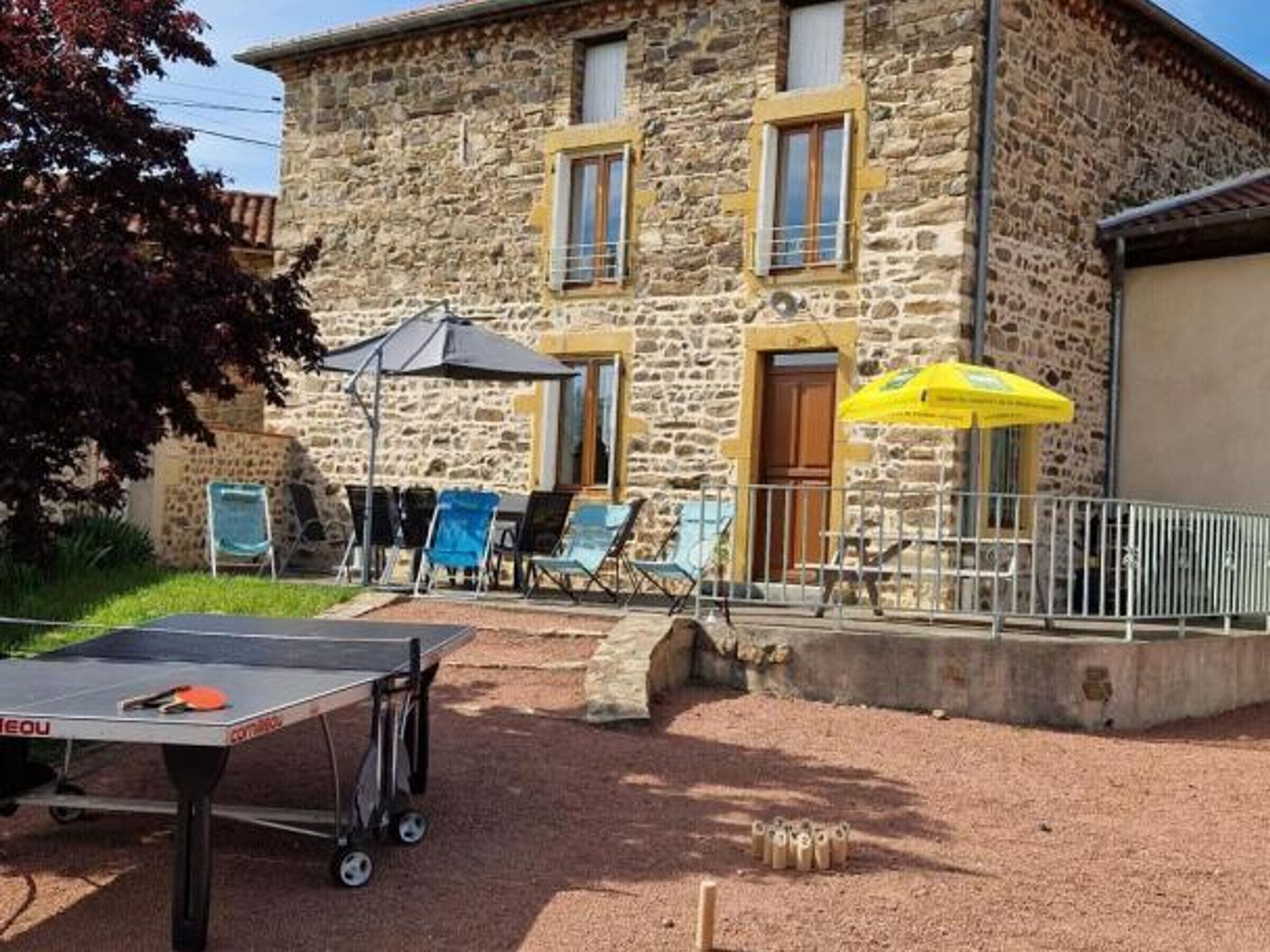 Un bâtiment en pierre doté d’un patio comprenant une table de ping-pong, des sièges d’extérieur et des parasols.