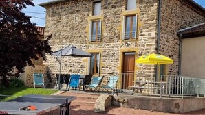 Ein Steinhaus mit einer Terrasse, auf der ein Tischtennisch betrieben werden kann und Sitzgelegenheiten sowie Sonnenschirme vorhanden sind.