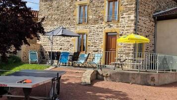Un bâtiment en pierre doté d’un patio comprenant une table de ping-pong, des sièges d’extérieur et des parasols.