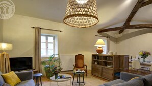 Una sala de estar acogedora con televisor, sofás, una mesa de centro, una silla, una lámpara y una estantería.