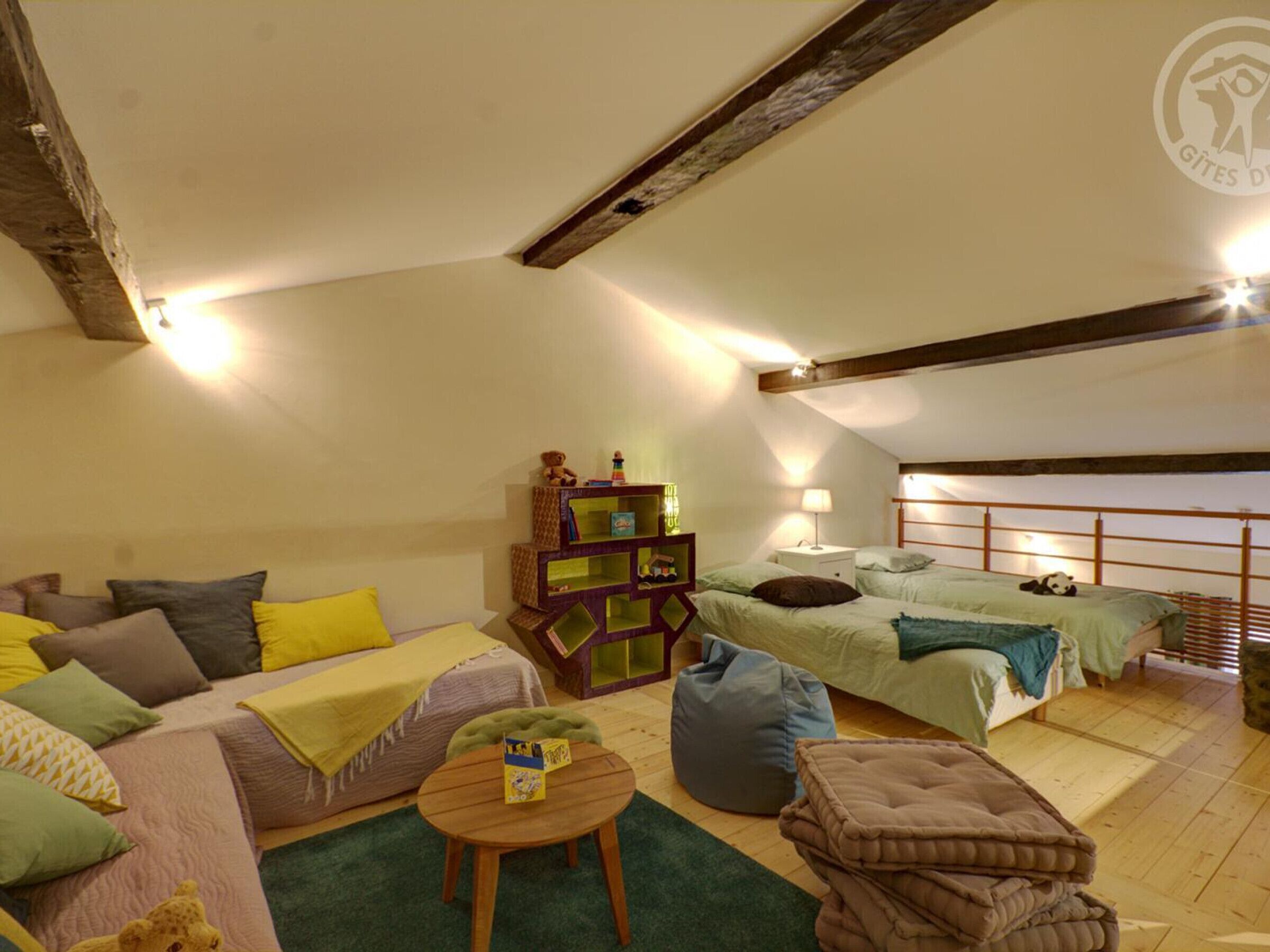 A cozy loft-style bedroom with a loft bed, a sofa with cushions, a small wooden table, and a colorful storage unit.