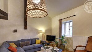 Una sala de estar con sofá, mesa de centro, televisor, lámpara, sillón y ventana.