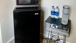 Una kitchenette compacta con refrigerador, microondas y una pequeña mesa con botellas de agua y dispensador.