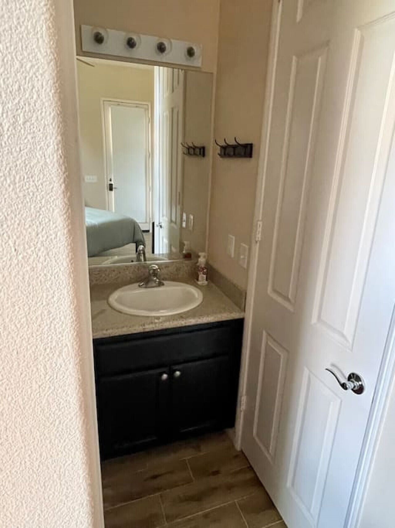 A bathroom with a vanity, sink, mirror, and a door with a handle.