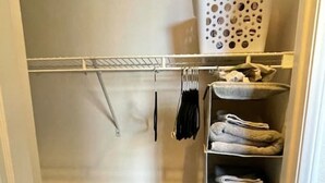 Un armario espacioso con repisas para ropa doblada, un tendedero y un basurero.