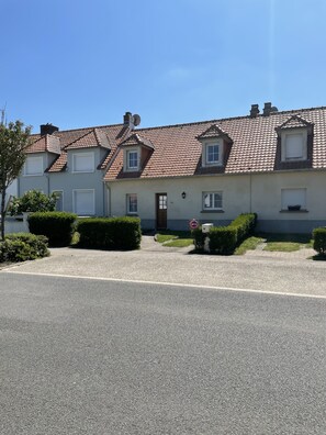 Ein zweistöckiges Gebäude mit einem Ziegeldach, einem zentralen Eingang und einem kleinen Garten mit Hecken.