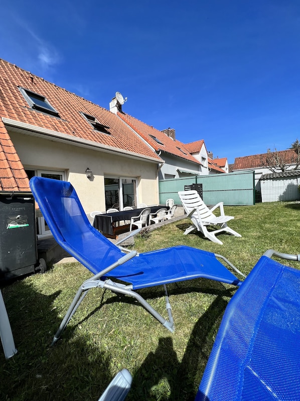 Ein Garten mit einem Haus, einer Rasenfläche und zwei blauen Gartenstühlen.