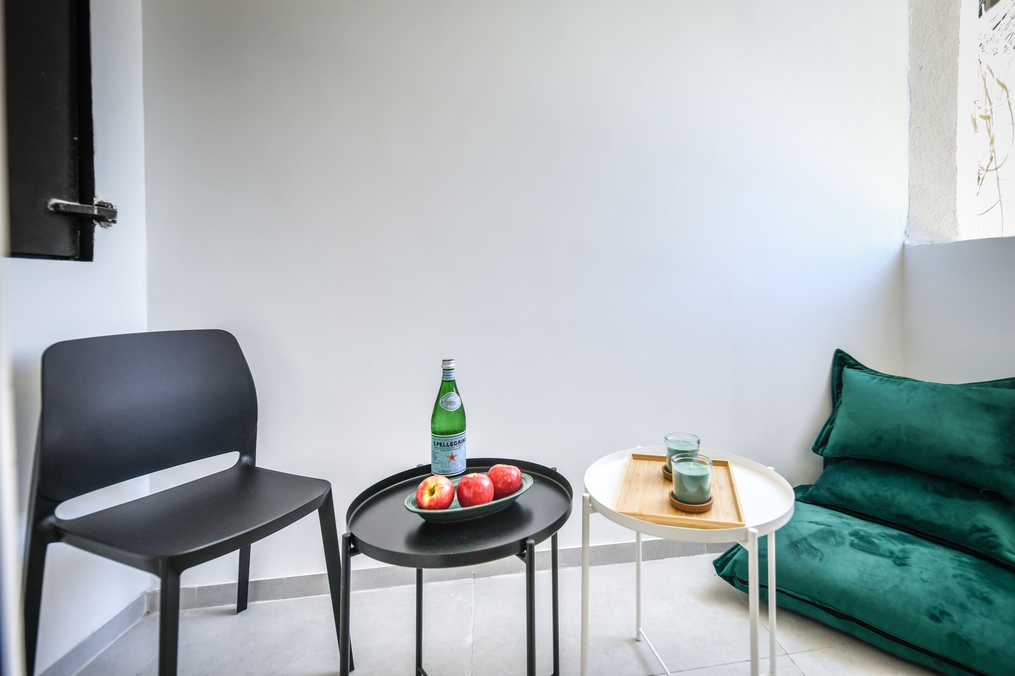 Een kleine, moderne kamer met een zwarte stoel, een tafeltje met een groene fles en appels, en een groene bank.