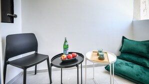 Pieni, moderni huone, jossa on musta tuoli, pieni pöytä, jonka päällä on vihreä pullo ja omenoita, sekä vihreä sohva.