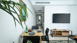 Moderni ruokailutila, jossa on puinen pöytä, mustat tuolit ja seinälle asennettu televisio.