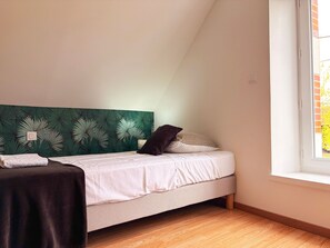 A bedroom with a bed, a headboard with a leaf pattern, a window, and a wooden floor. - Charming Cottage Near Beauval Zoo & Loire Castles - Private Courtyard & Bike Access (La Vernelle)