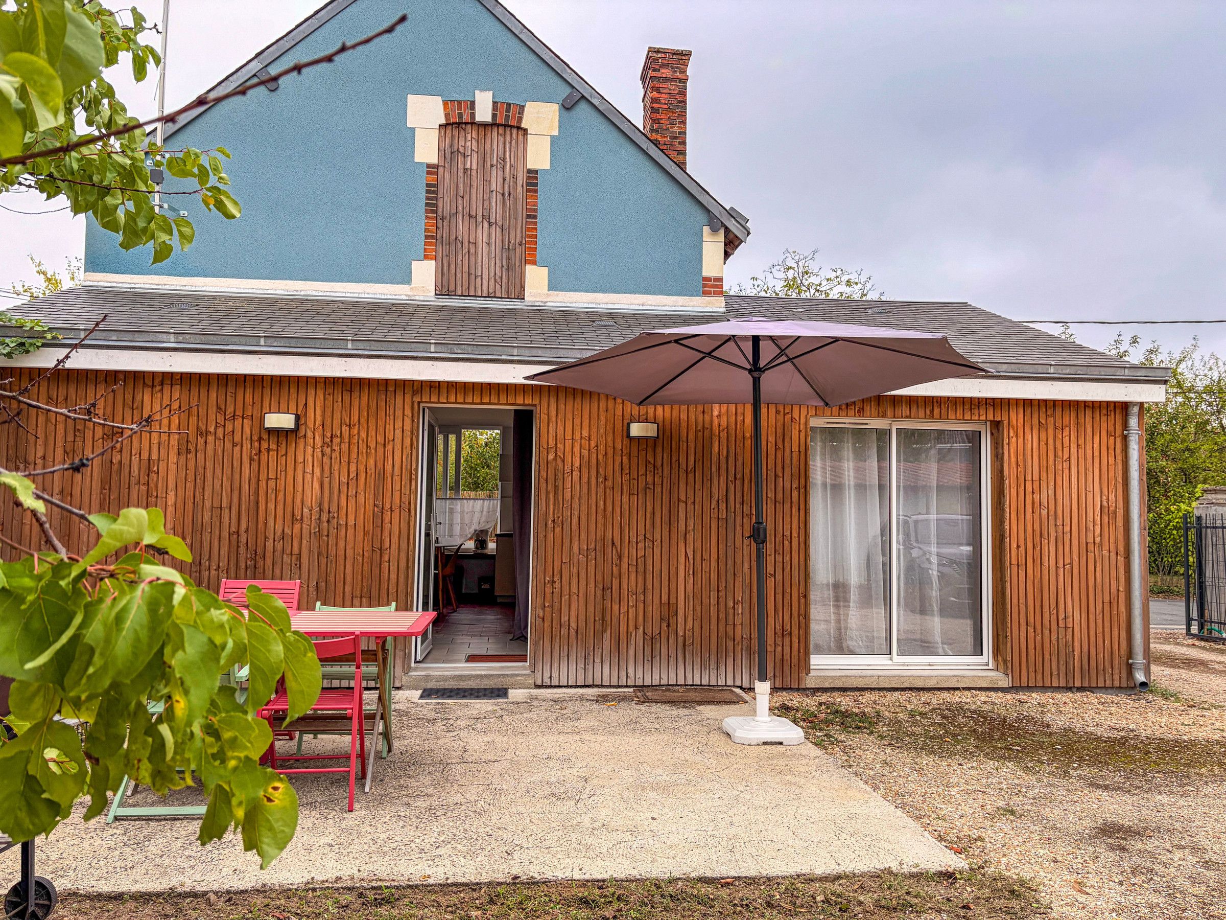 A house with a blue exterior, wooden siding, a patio with a table and chairs, and a large umbrella.