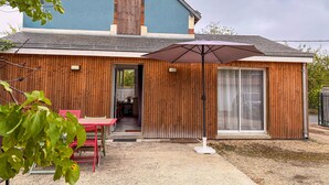 Une maison à l’extérieur bleu, avec un revêtement en bois, une terrasse dotée d’une table et de chaises, et un grand parasol.