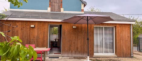 A house with a blue exterior, wooden siding, a patio with a table and chairs, and a large umbrella.