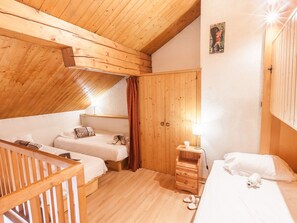 A cozy attic bedroom with wooden beams, two beds, a small wooden nightstand, and a red curtain.