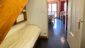A bedroom with a wooden staircase, a bed, and a view into a dining area with a table and chairs. - Savoyard duplex for 6 in Méribel center with wifi (Méribel)