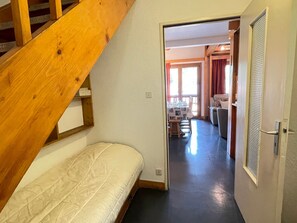 A bedroom with a wooden staircase, a bed, and a view into a dining area with a table and chairs.