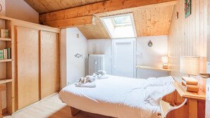 A bedroom with a wooden ceiling, a skylight, a bed, a radiator, and a shelf with books. - Savoyard duplex for 6 in Méribel center with wifi (Méribel)
