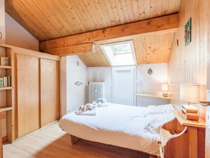 A bedroom with a wooden ceiling, a skylight, a bed, a radiator, and a shelf with books.