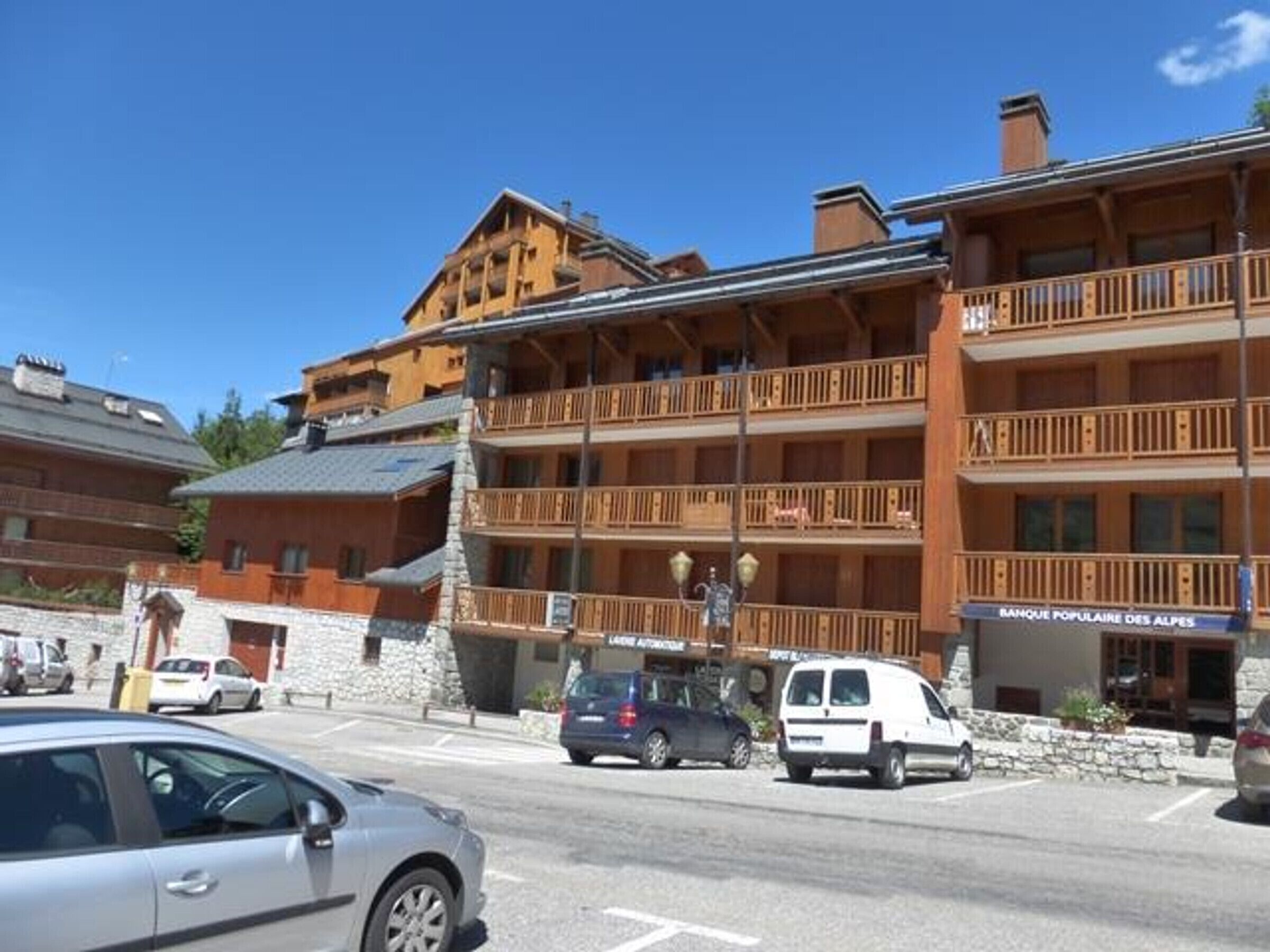 Ein mehrstöckiges Hotel mit Balkonen, einem Schild für 'Banque Populaire des Alpes' und Autos vor der Fassade.