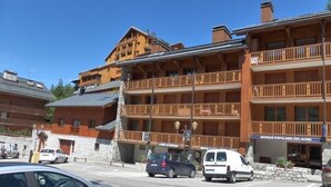 A multi-story hotel with balconies, a sign for 'Banque Populaire des Alpes', and cars parked in front. - Savoyard duplex for 6 in Méribel center with wifi (Méribel)