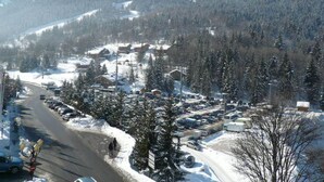 Une ville de montagne enneigée, avec une rue principale, des voitures garées et des bâtiments.