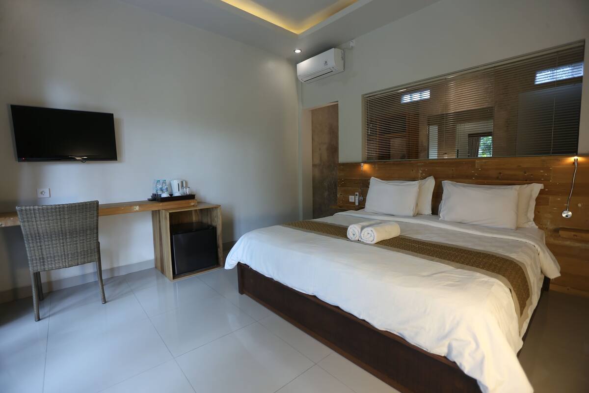 Una habitación de hotel con cama, escritorio, silla, televisor y aire acondicionado.