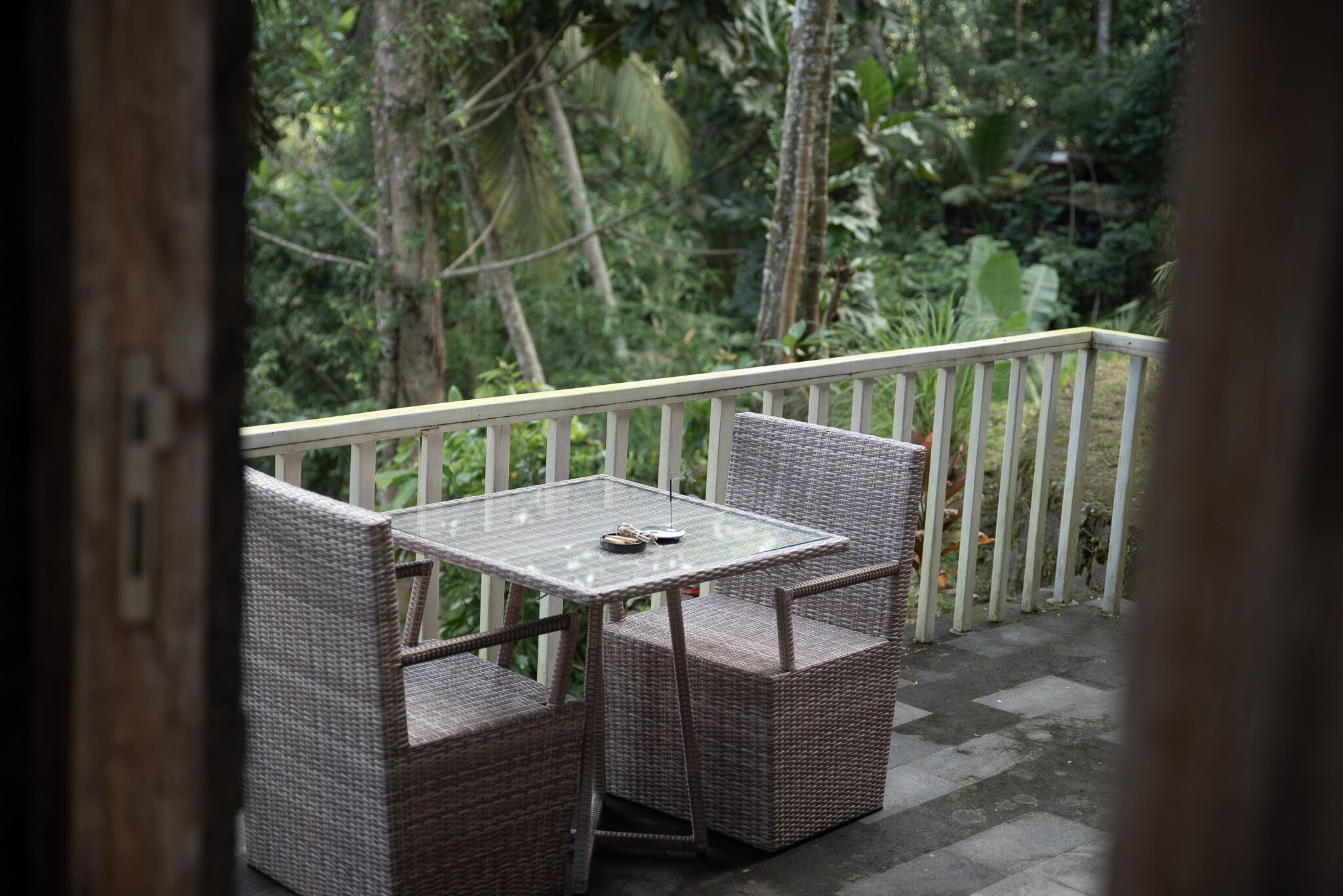 Un balcon agrémenté de meubles en osier et d’une table en verre, entouré d’une végétation luxuriante.