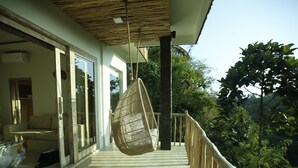 A balcony with a hanging chair, a sofa, and a glass door leading to a room. - Angsoka Bungalow (Ubud)