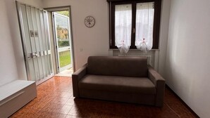 Une pièce avec un canapé, une horloge au mur et une fenêtre avec des rideaux.