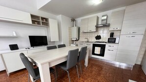 Une cuisine moderne avec des meubles blancs, une table à manger avec des chaises et un téléviseur.
