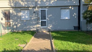Un chemin menant à un bâtiment doté d’un toit plat, d’une porte centrale et de fenêtres équipées de stores.
