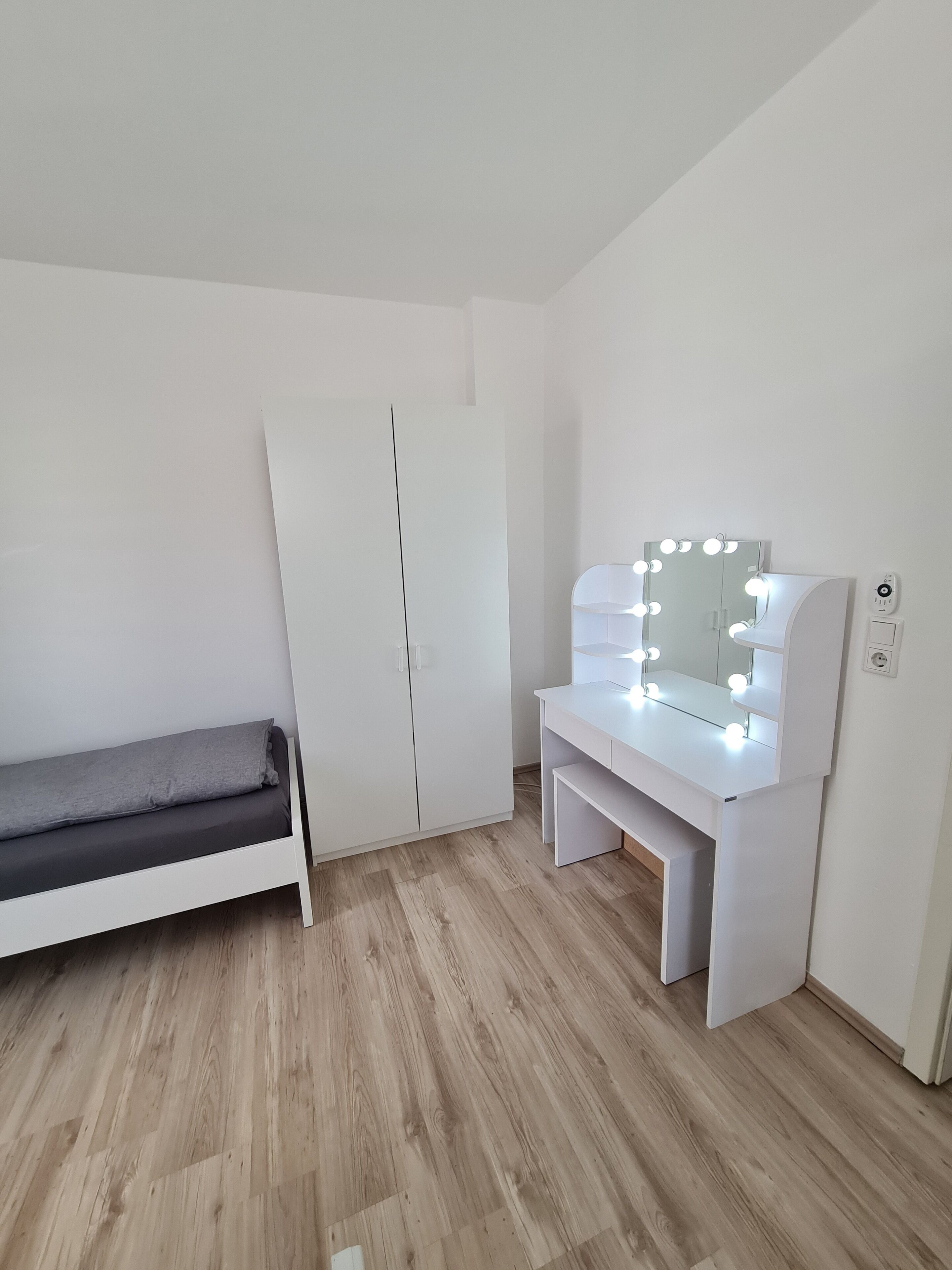 Une chambre à coucher comprenant un lit, une coiffeuse avec éclairage, une armoire et un miroir.